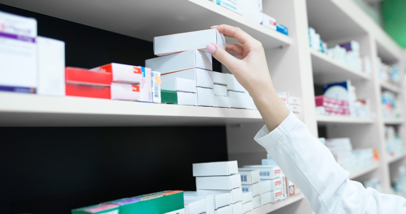 Closeup view of pharmacist hand taking medicine box from the shelf in drug store.